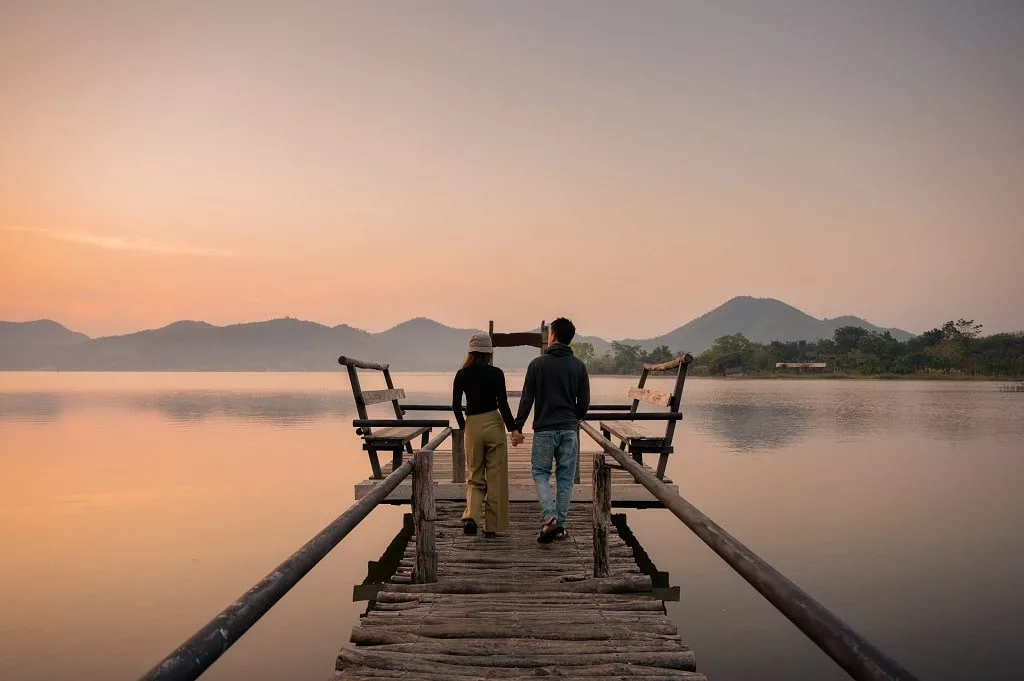 Young couple walking and holding hands on wooden bridge at sunset.