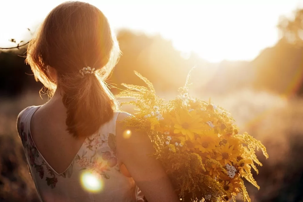 Girl in the field carrying flowers at sunset.