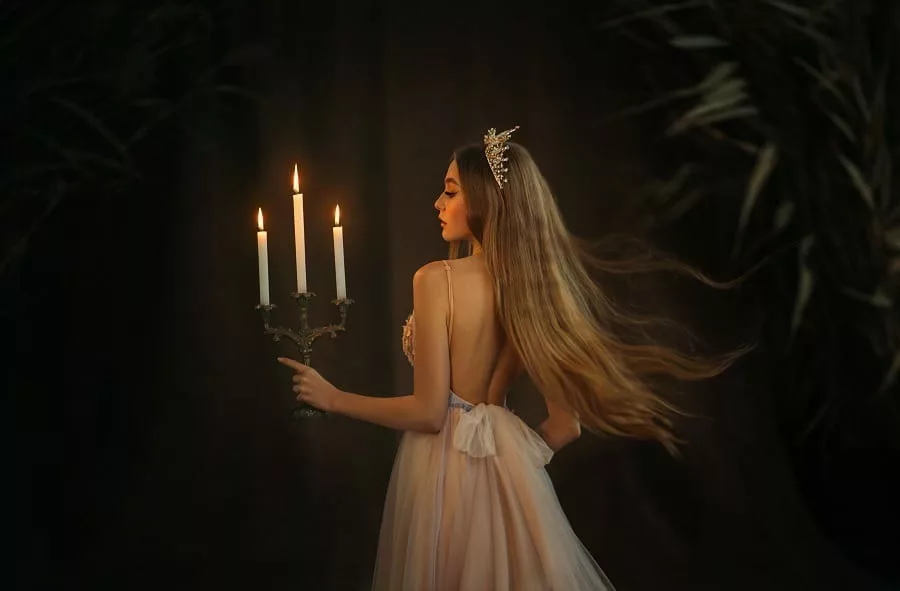 Beautiful medieval queen in white gown, holding a candlestick with burning candles in hand.