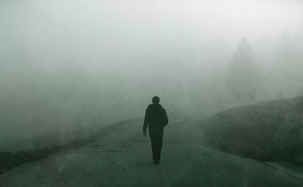 Man walking alone on grunge textured foggy rural road.