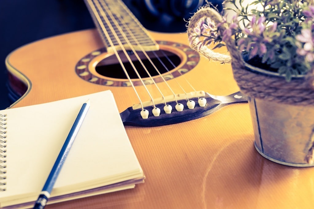 Guitar and notebook with a beautiful flower bucket.
