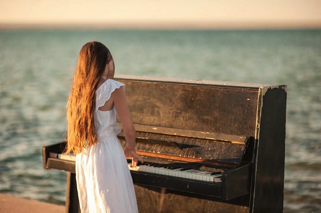 Beautiful girl in a white dress plays the piano on the pier by the sea.