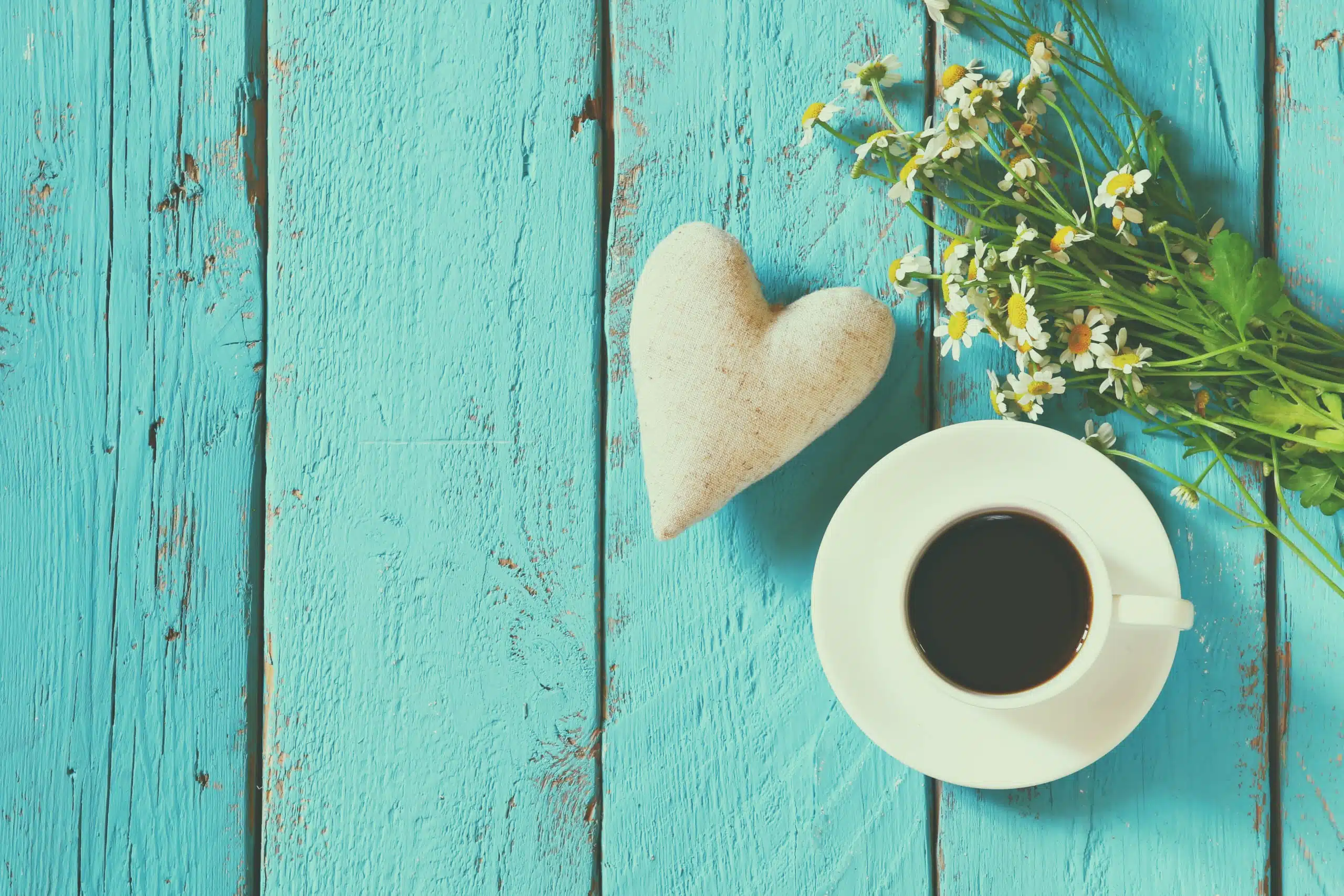 White heart and a cup of coffee on blue wooden table.