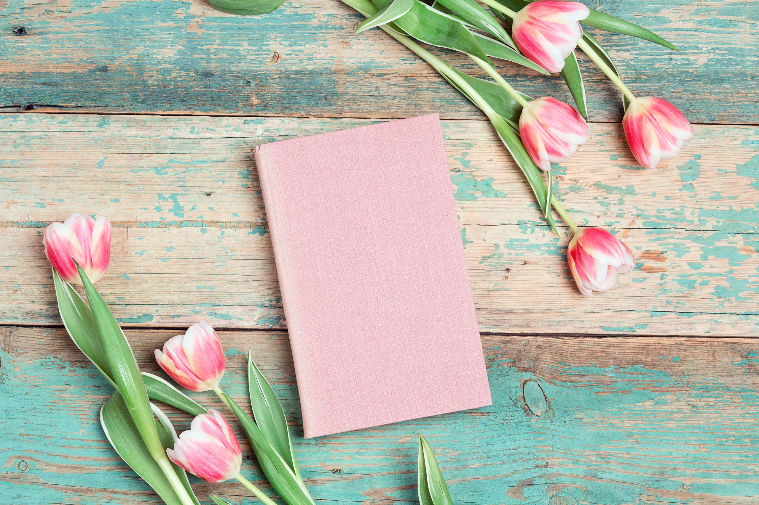 Tulip flowers and pink book on vintage wooden table.