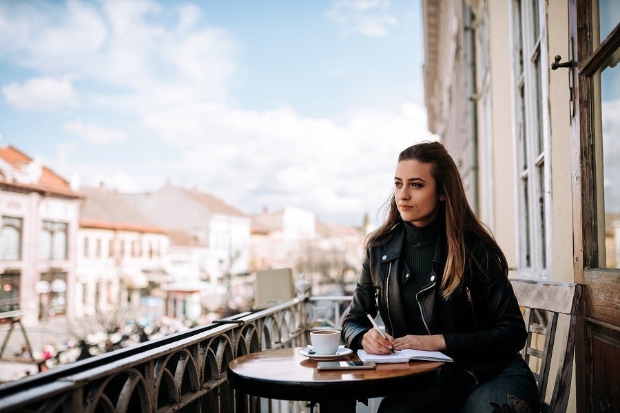 Lovely girl writing outdoors in the café with scenic view.