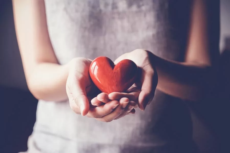 Close-up woman's cupped hands holding a red heart.