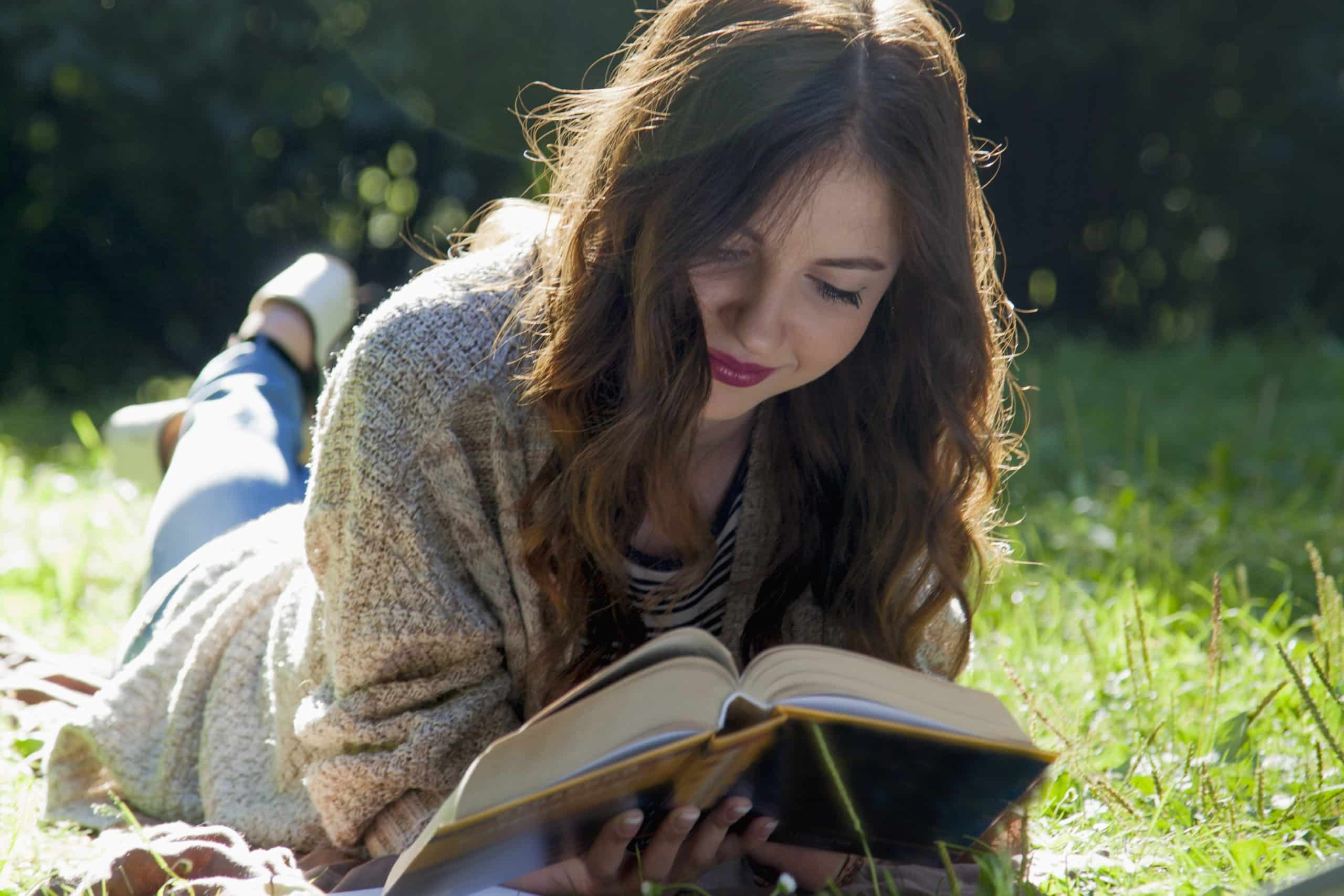 Beautiful young woman reading a book outdoors.