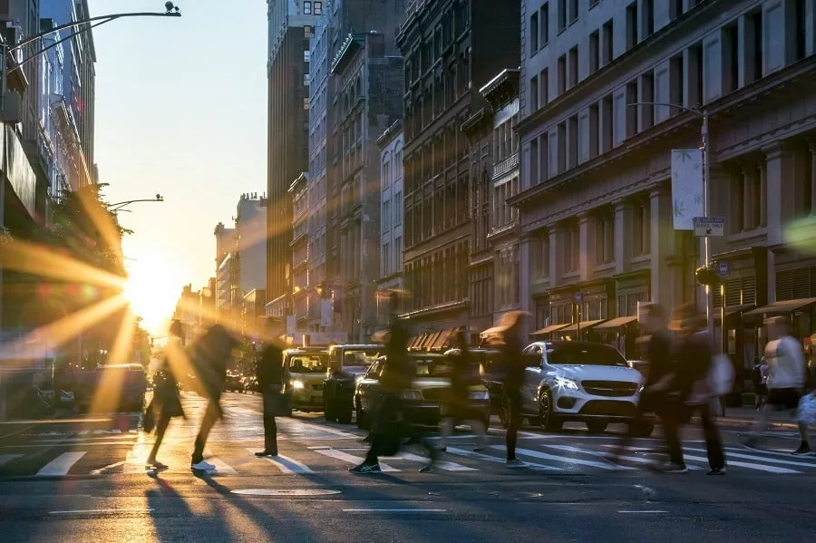 Rays of sunlight shine on the busy people walking across an intersection in Midtown Manhattan. 