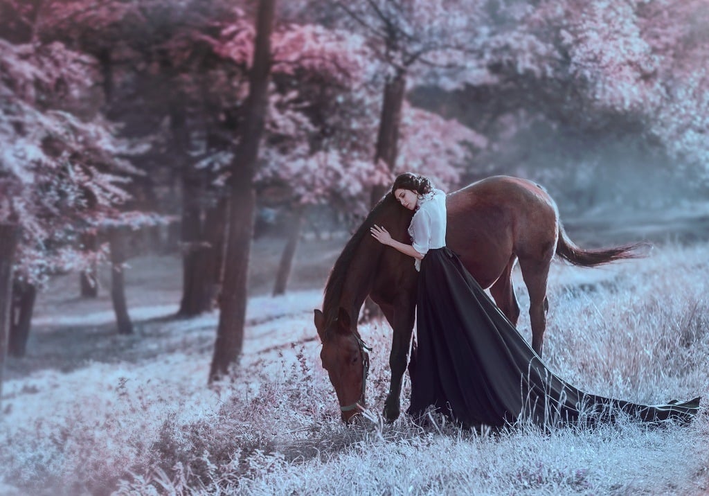 A young princess in a vintage dress with tenderness and love, hugs her horse.
