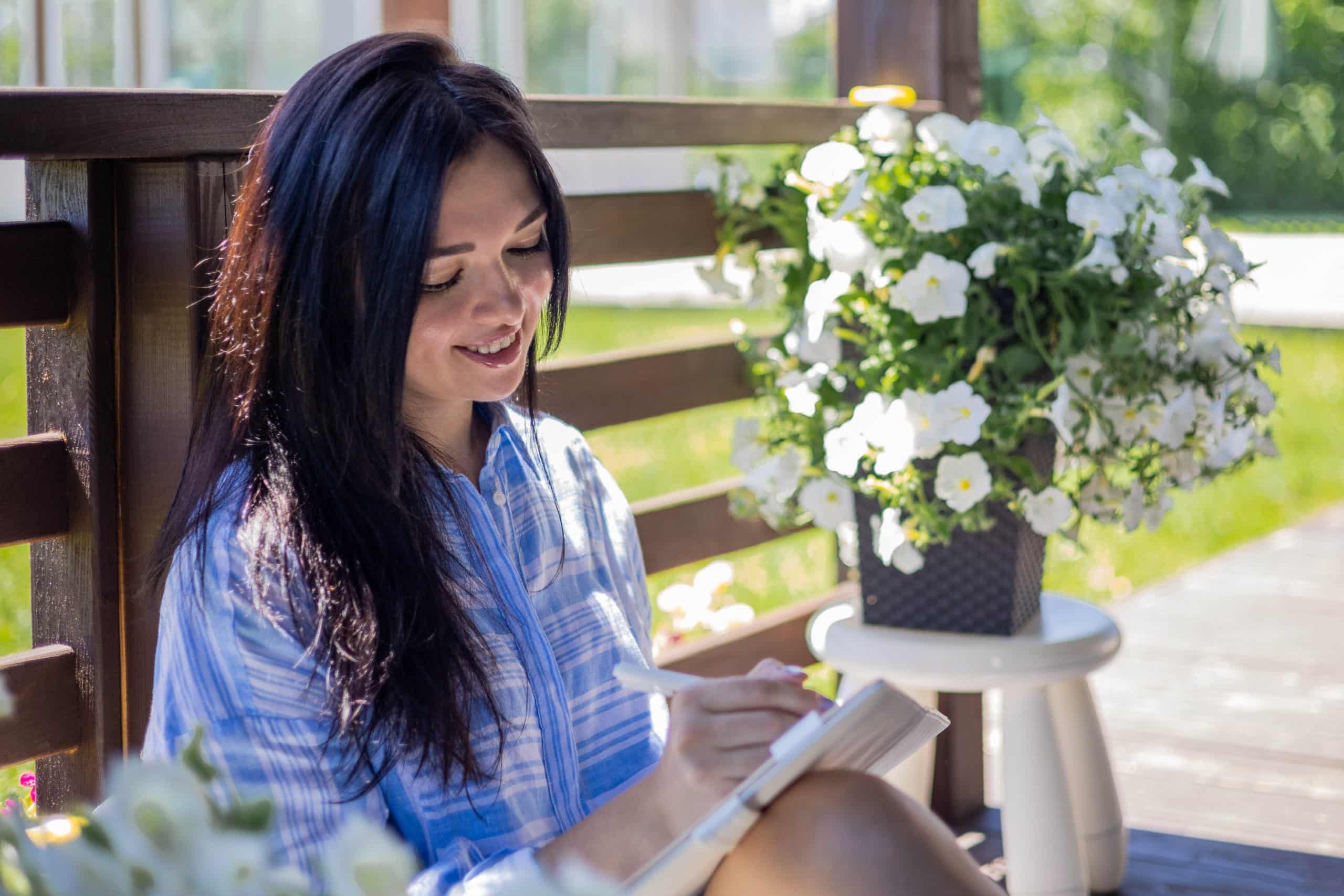 Woman smiling on her notebook while sitting on outdoor summer terrace at countryside.