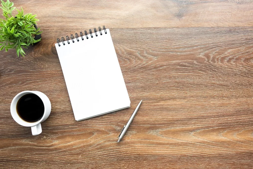 Wood office desk table with blank notebook page with pen and a cup of coffee.