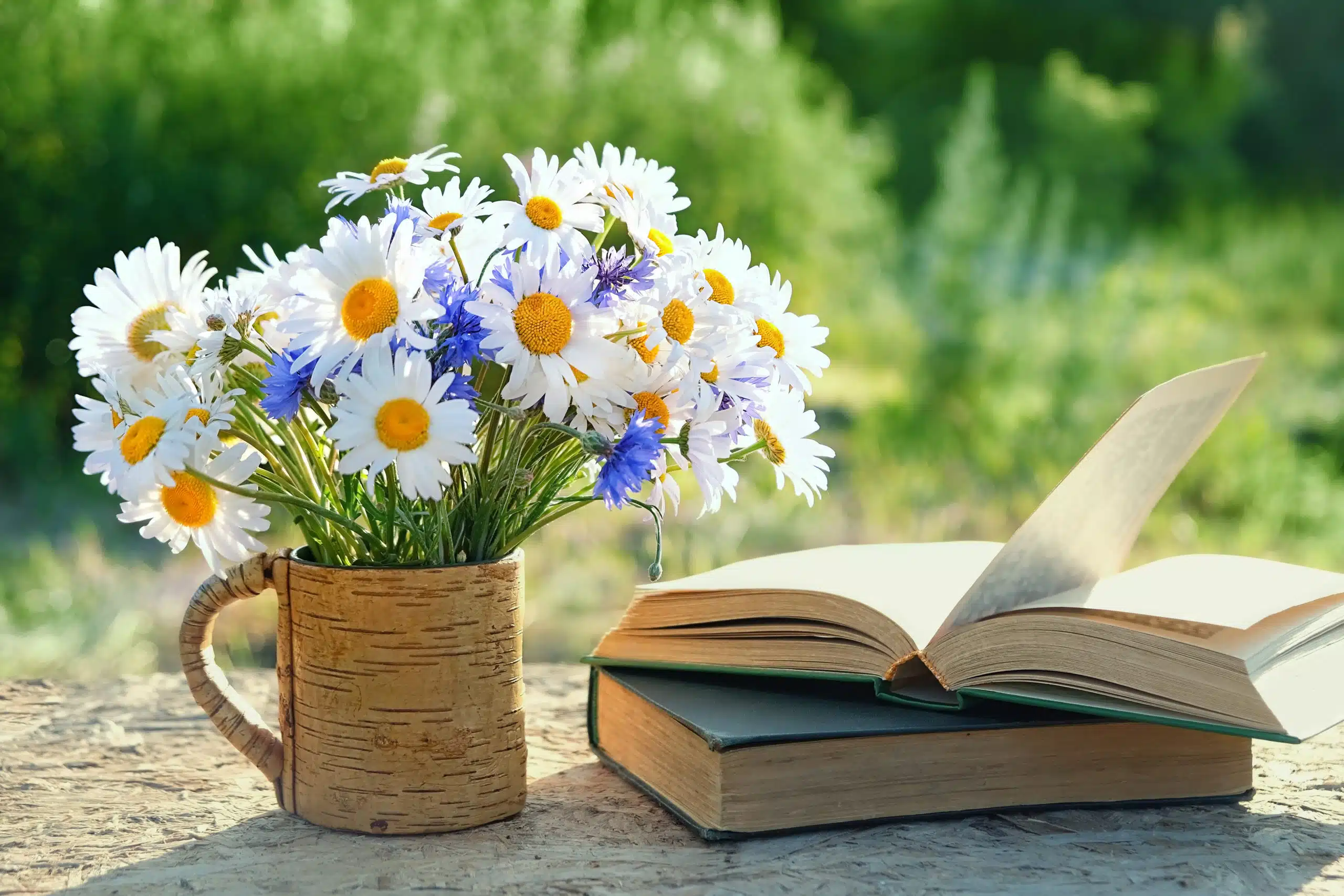Flowers bouqet in rustic cup and old books on table in the garden.