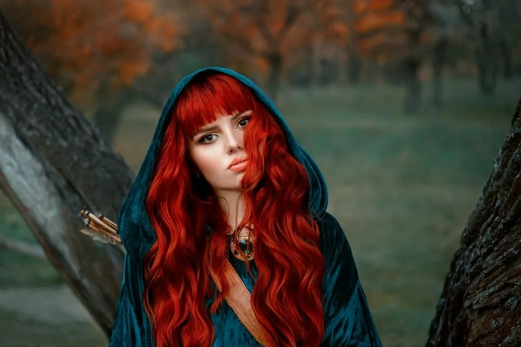 Attractive red-haired female warrior with fierce brown eyes, wearing blue velvet cloak with hood on her head.