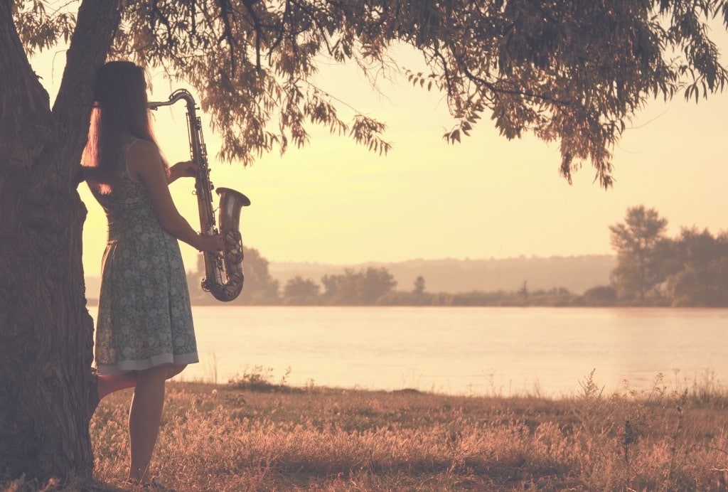 Vintage woman standing near a tree playing a saxophone.