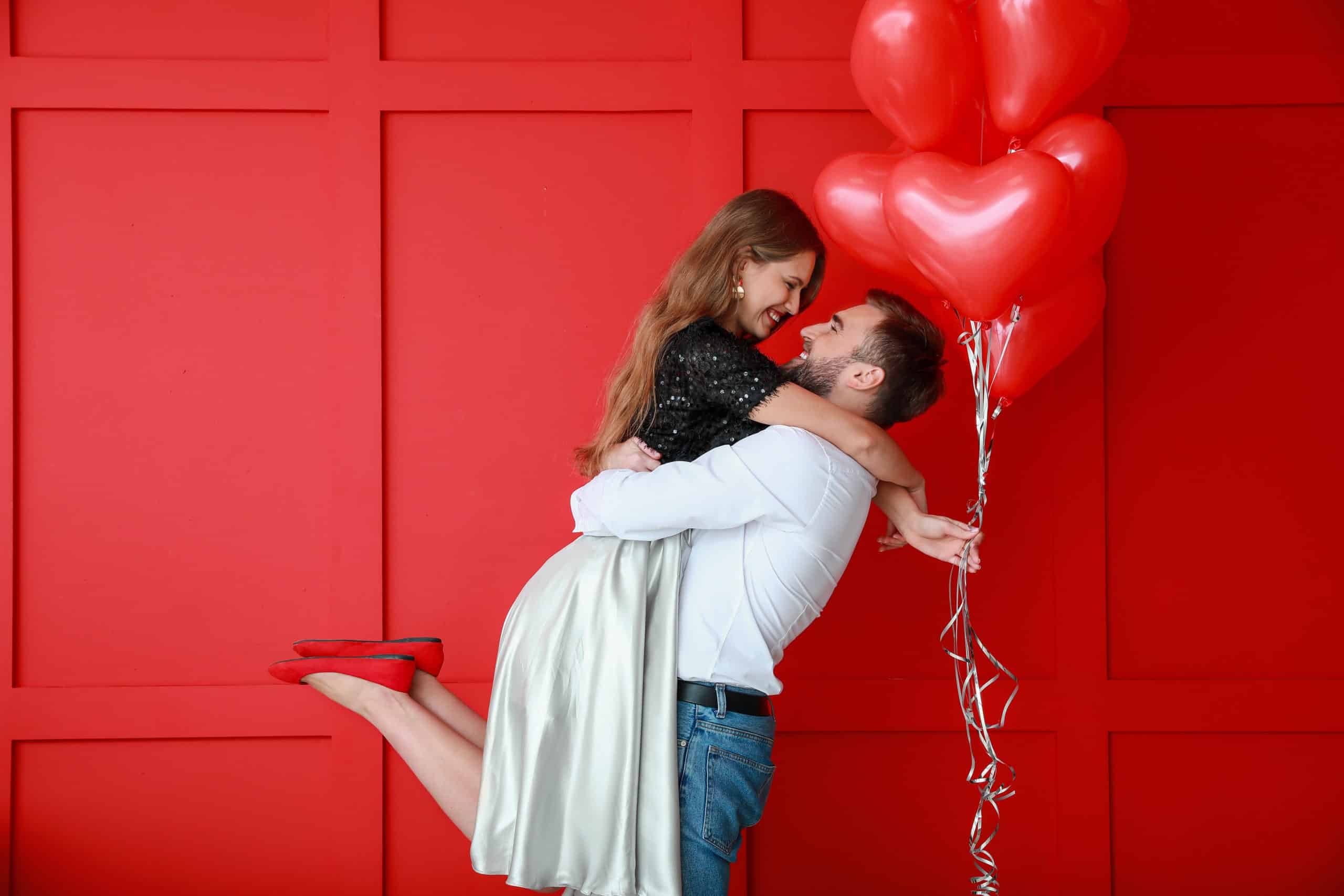 Happy young couple with heart-shaped balloons on color background, Valentine's Day celebration.
