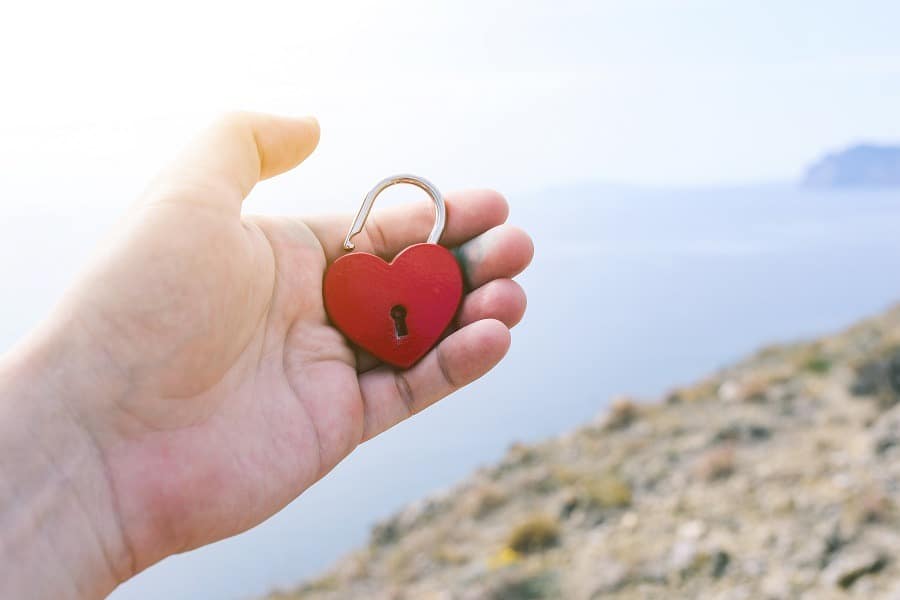 Male hand holding a heart lock with the sea in the background.