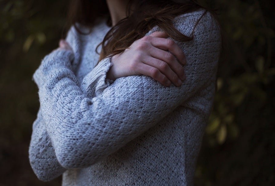 A young woman hugging herself arms crossed on her chest as if in emotional pain. 