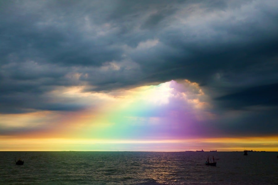 Rainbow splashes colors on the dark cloud at sea.