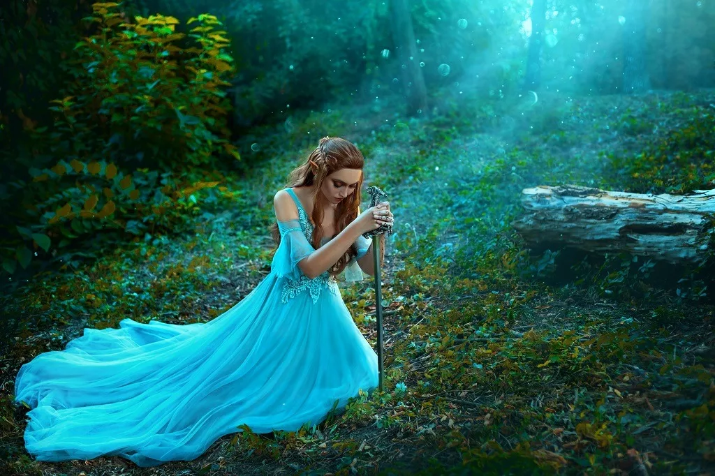 Fantasy princess warrior sits in forest on green grass holding weapon medieval sword in hands.