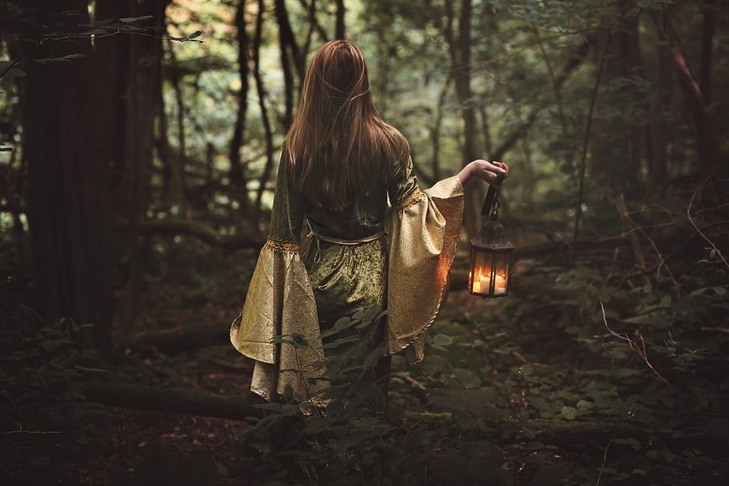 Mysterious woman walking toward the fairy forest carrying a lighted lantern.