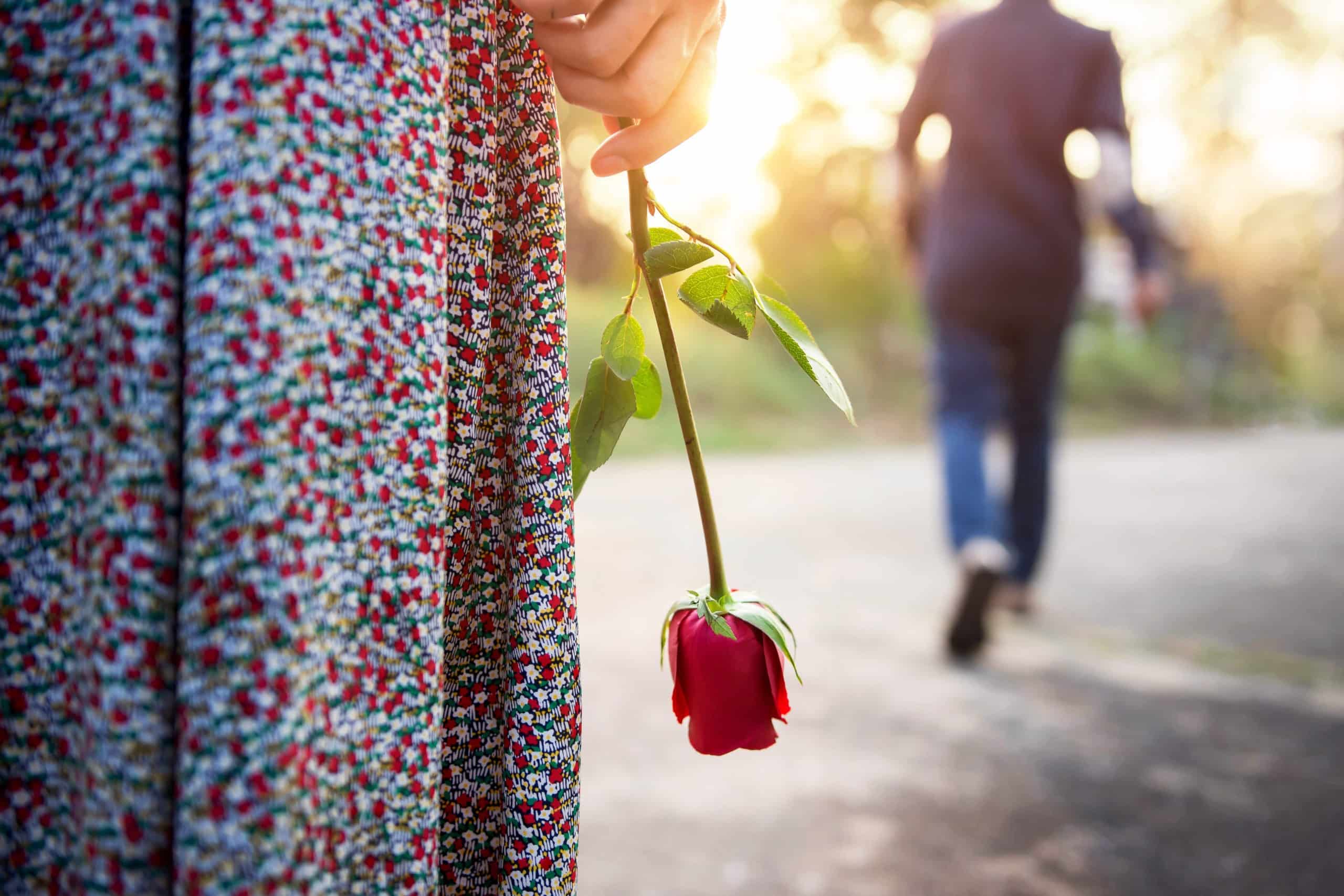 Man walking away, woman arms down standing behind with a rose in hand