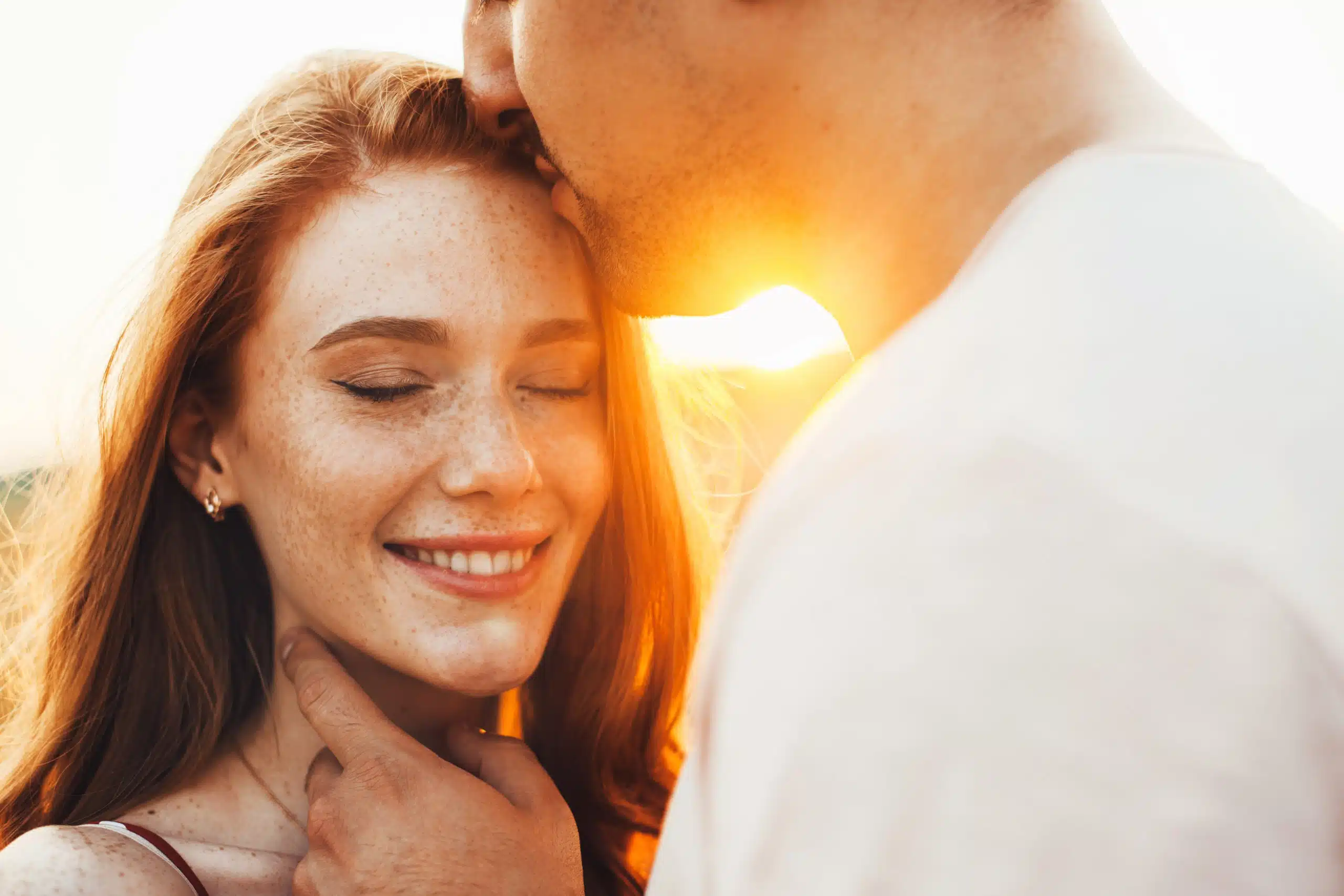Freckled woman smiling as she is kissed on the forehead by her boyfriend
