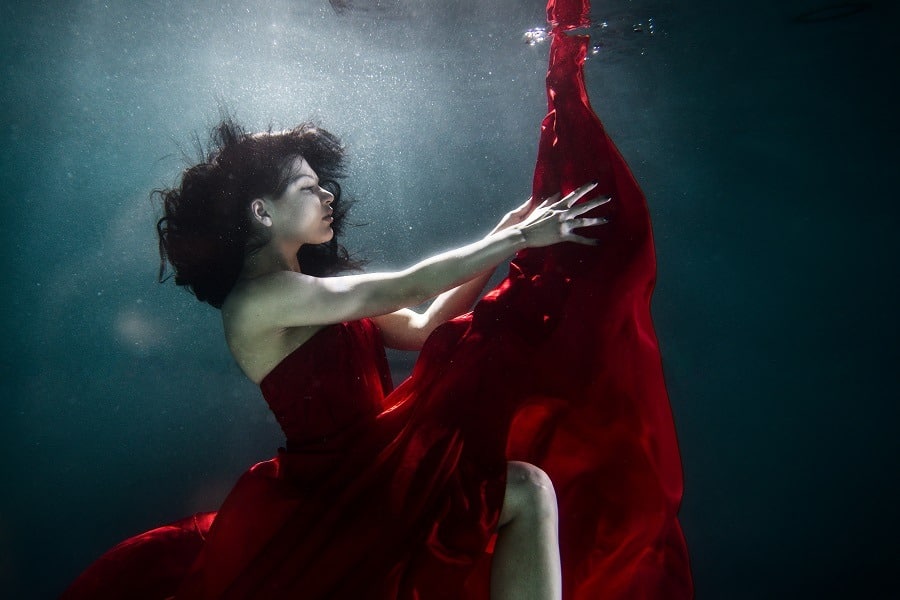 Stunning woman in red dress underwater, dark dreamy background.