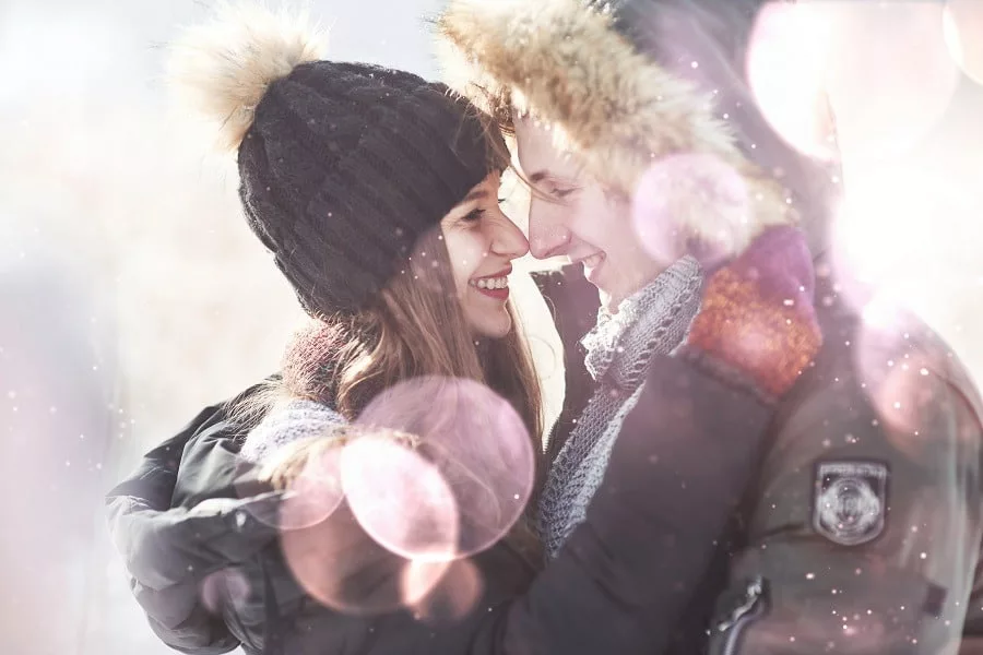 Young happy couple in love embrace in snowy winter cold forest.