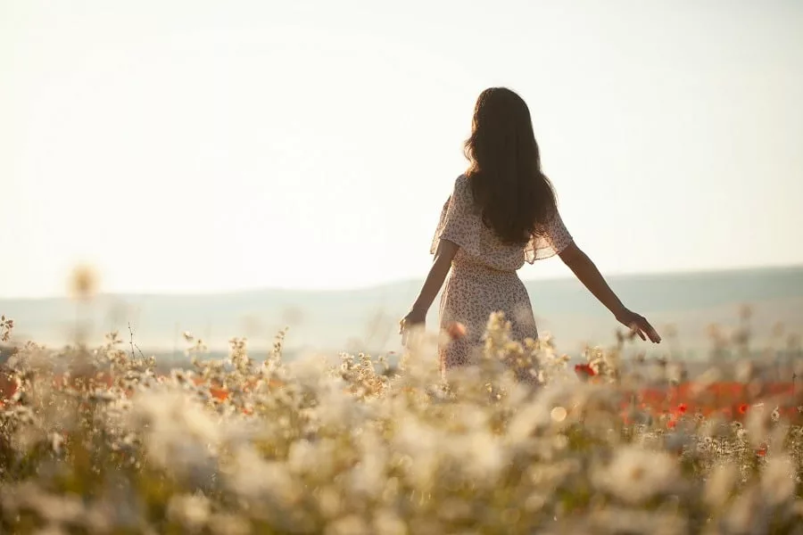 Beautiful girl in summer dress walks in a flower field.