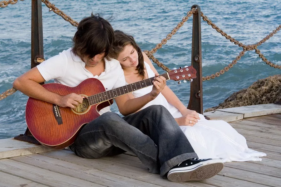 Man playing guitar for her woman by the sea.