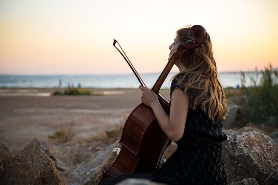Young beautiful girl with her cello looking dreamily at the ocean.