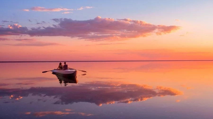 A couple in love look at beautiful sunset in a rowing boat on the lake. 