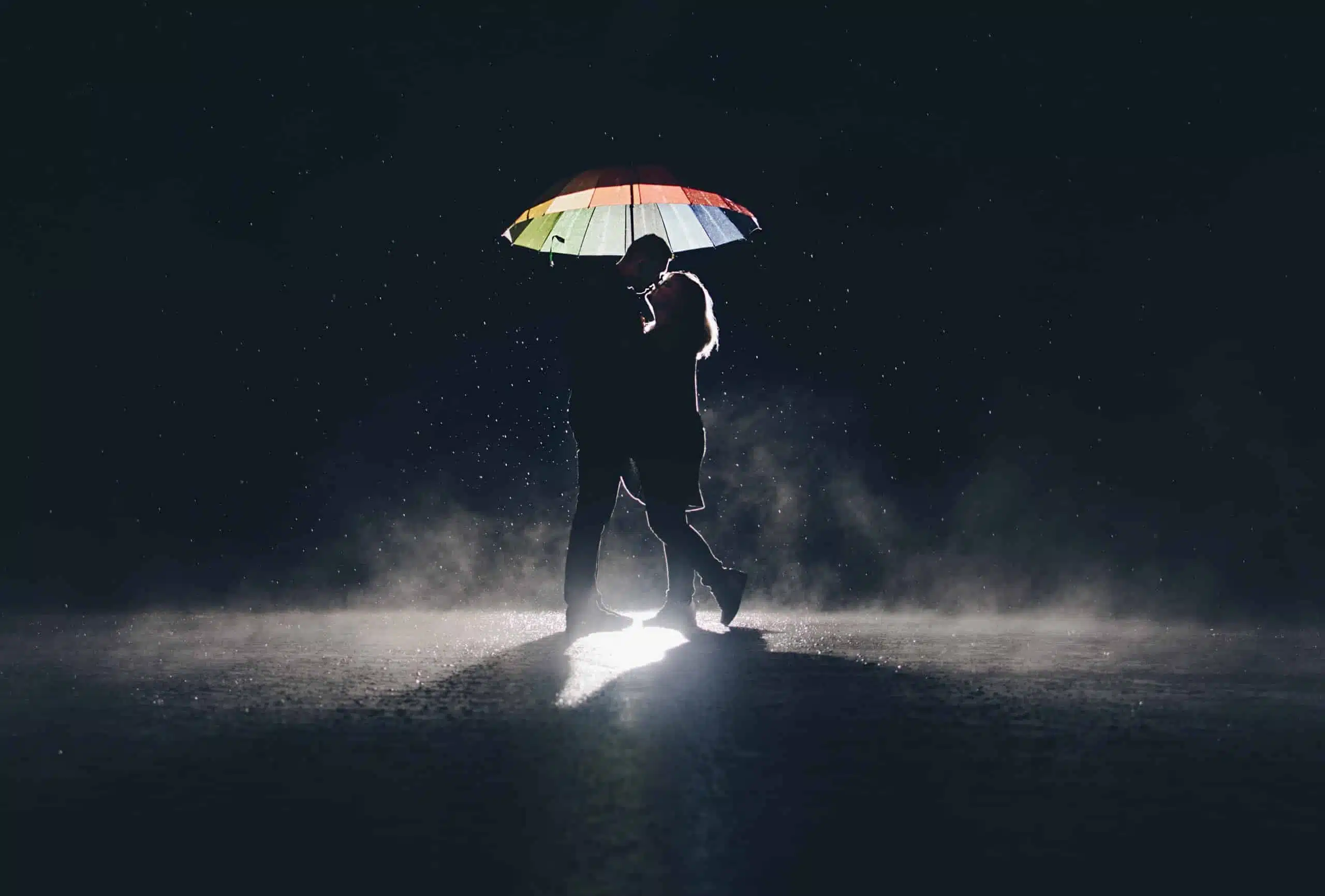 Lovers under at colorful umbrella in the rain at night.