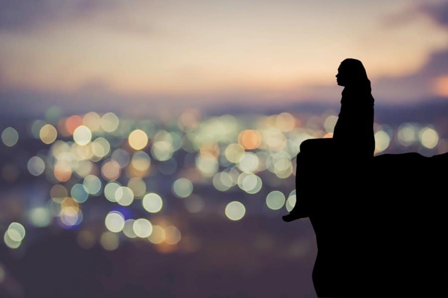 Silhouette of woman sitting alone with blurred view of city lights at night.