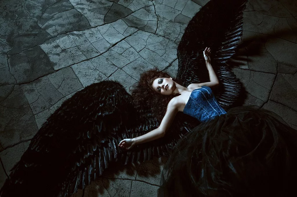 Angel with black wings lying on the ground.
