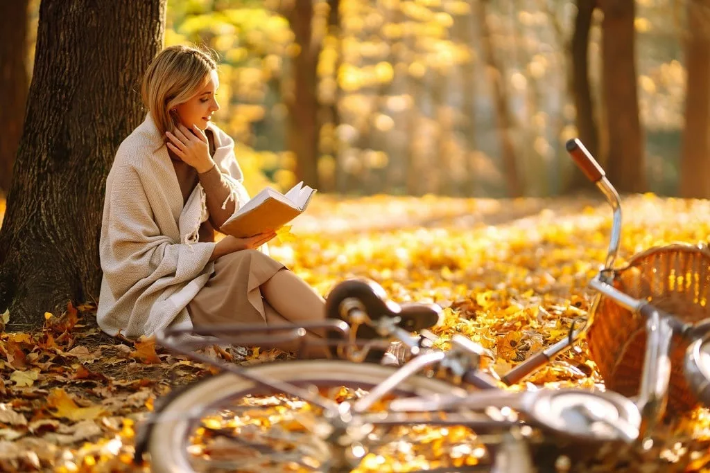 Stylish woman reading a book in the autumn park, enjoying soliture with nature.