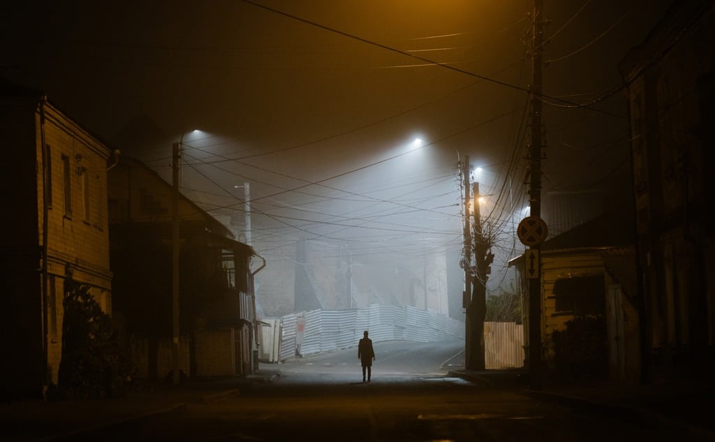 Lonely woman walking in a foggy old city in city street lights