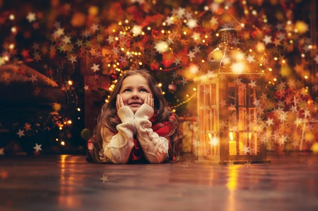 Cheerful little girl lies on the floor in front of Christmas tree with bright lights.
