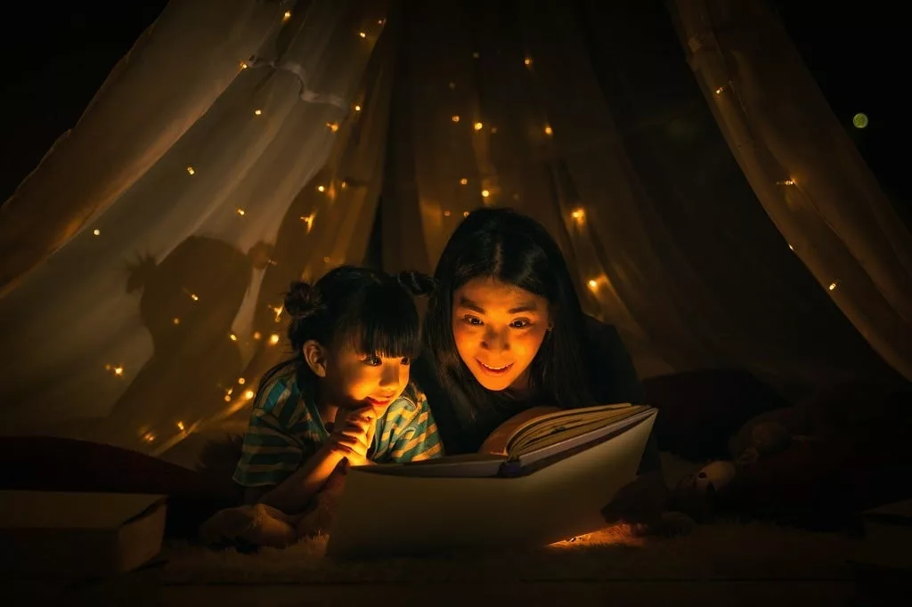 Mom and daughter read bedtime stories fairytale together before going to bed.