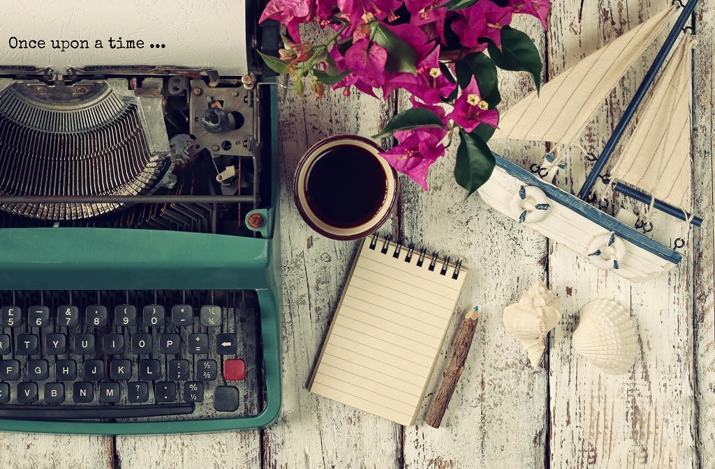 Vintage typewriter with phrase "once upon a time" a cup of coffee and old sailboat on wooden table.