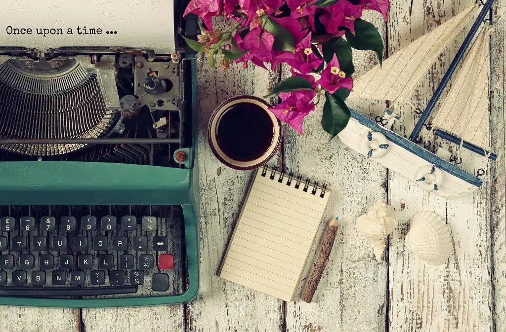 Vintage typewriter with phrase "once upon a time" a cup of coffee and old sailboat on wooden table.