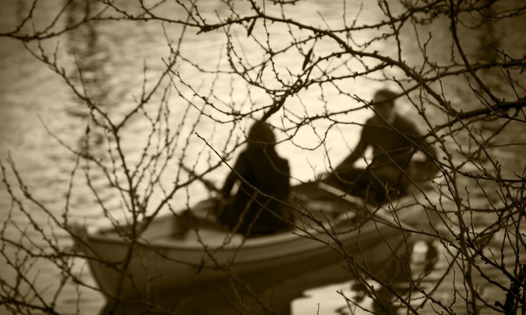 Man and woman on the boat  on river behind leafless trees.