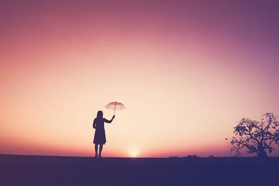 The silhouette of the lonely young woman holding an umbrella on the cliff at the sunset/
