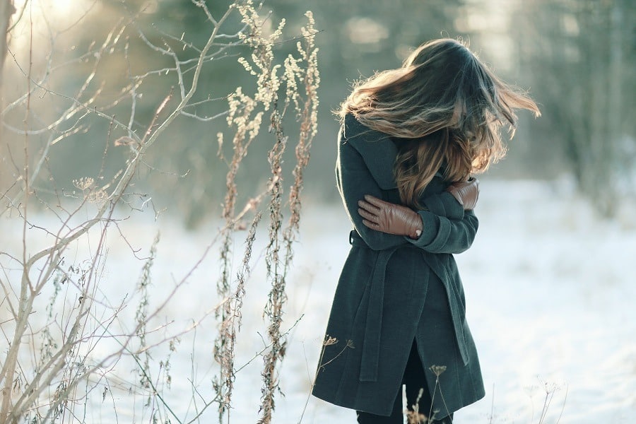 Woman outdoor in winter in emotional pain, hugging herself tightly.