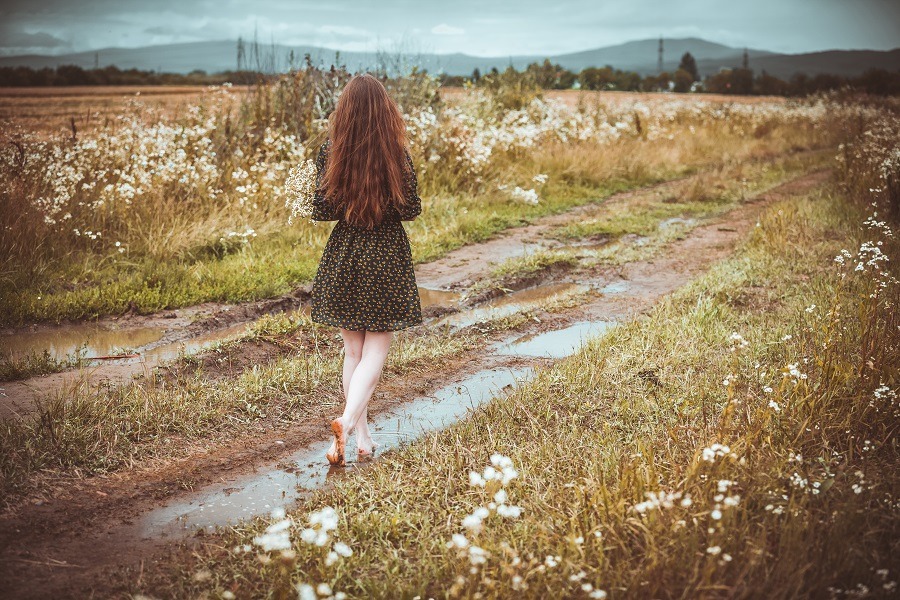 Lonely girl going on rural road with wild flowers in the background.