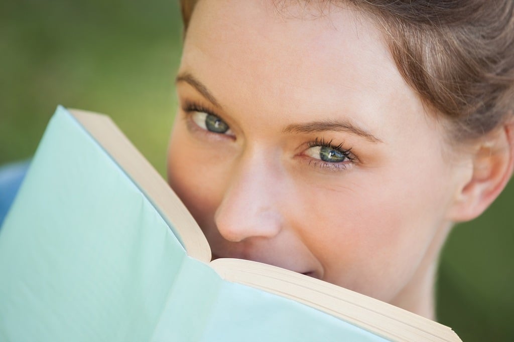 Beautiful woman with book covering her mouth.