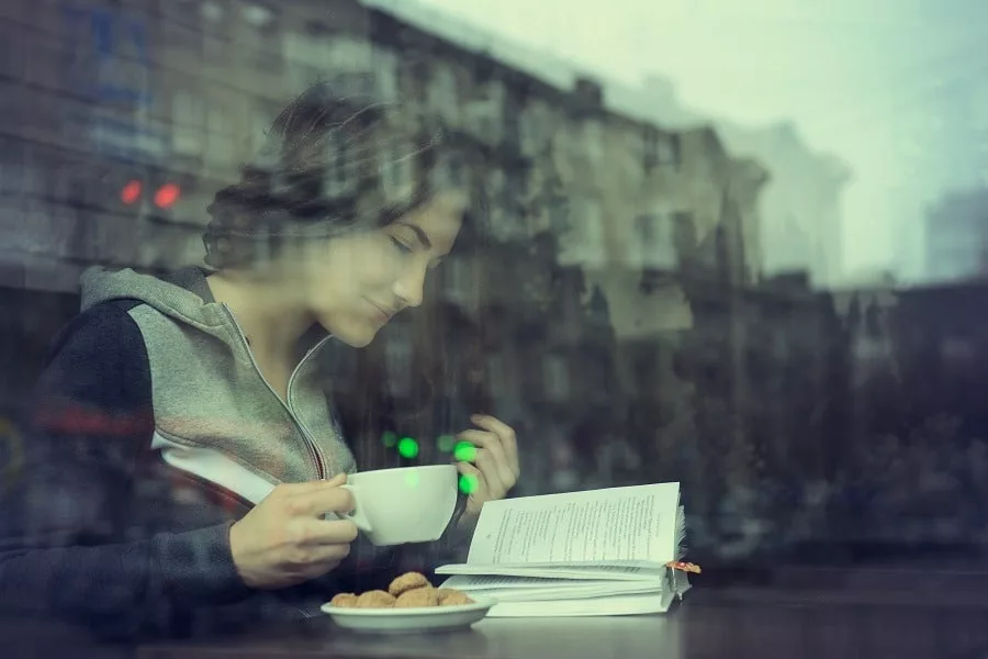 Young woman drinking coffee while reading poetry indoor.