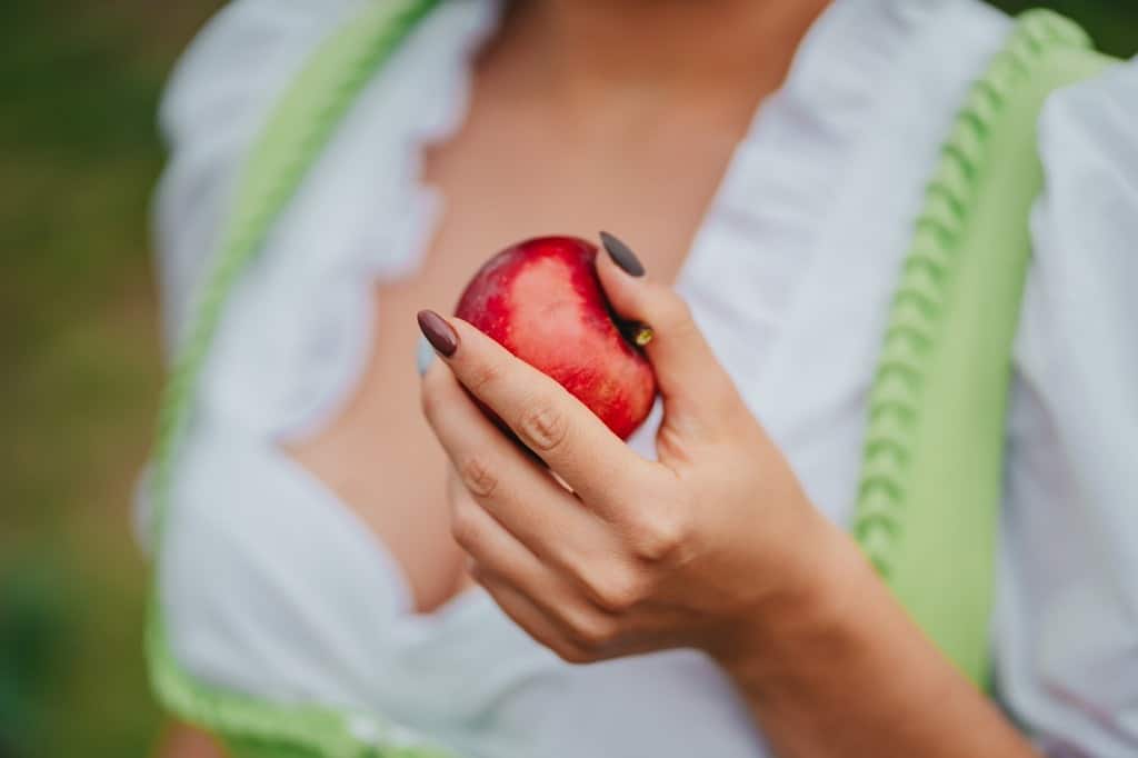 Woman holding a red apple as symbol of temptation or poison.