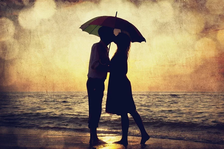 Couple kissing under umbrella at the beach in sunset.
