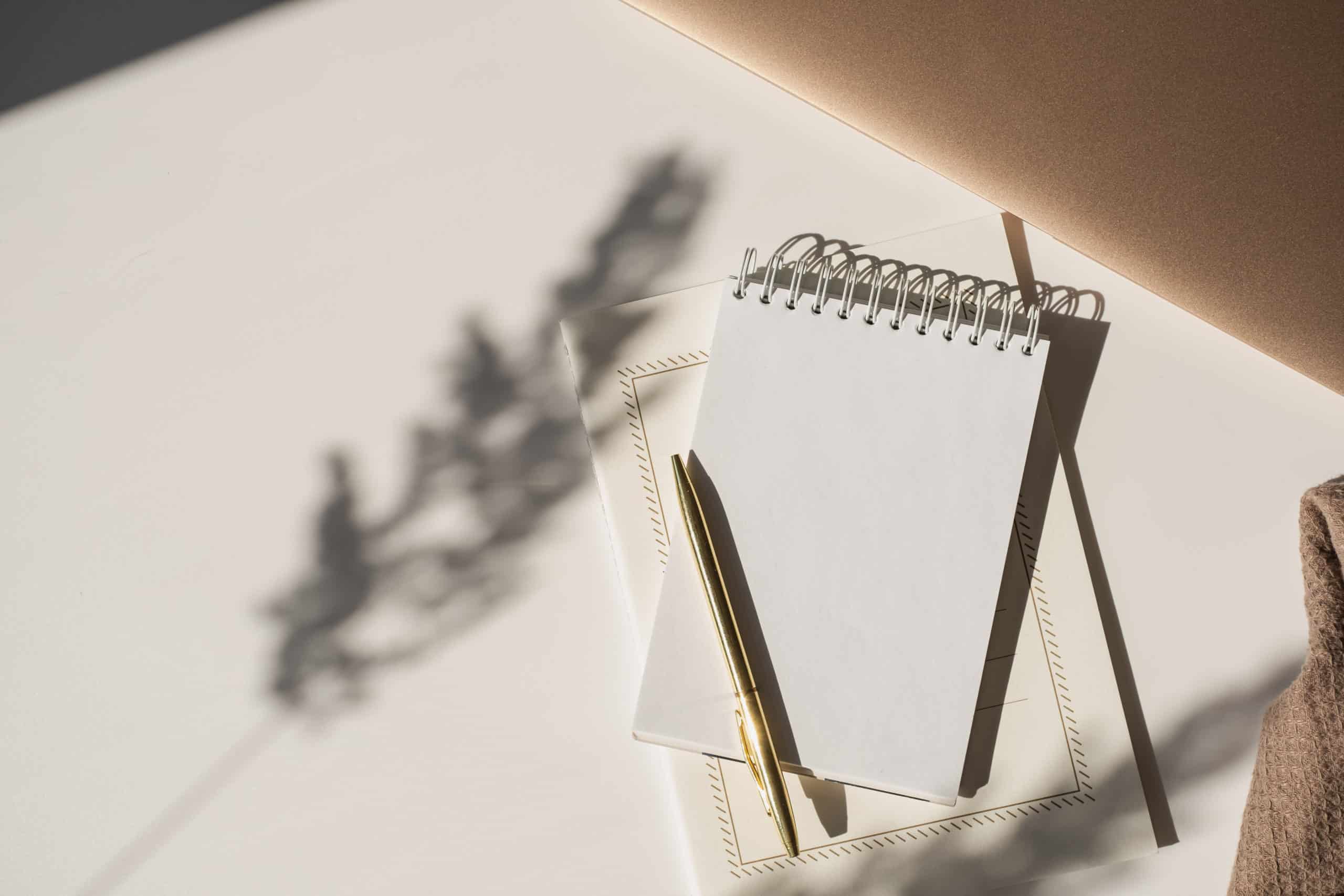 Blank spiral notebook, stationery paper, and pen in flowers sunlight shadow